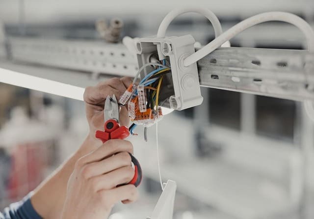 Electricista realizando conexiones de cableado en una caja de conexiones eléctricas.