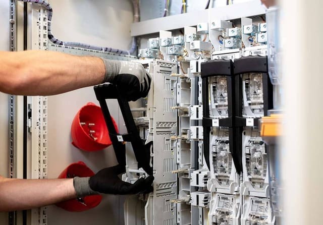 Técnico realizando tareas de mantenimiento en un cuadro eléctrico industrial con fusibles y sistemas de protección.