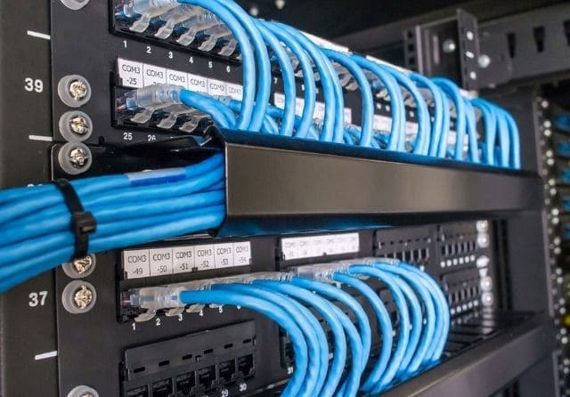 Rack de comunicaciones con cableado de red Ethernet azul conectado a paneles de parcheo.