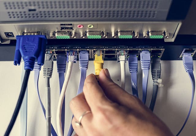 Una mano conectando un cable Ethernet a un switch de red con múltiples conexiones de datos.